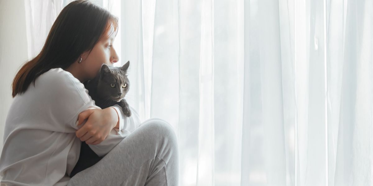 Imagen de una mujer triste mientras está sentada con un gato, posiblemente indicando un momento de consuelo o apoyo.