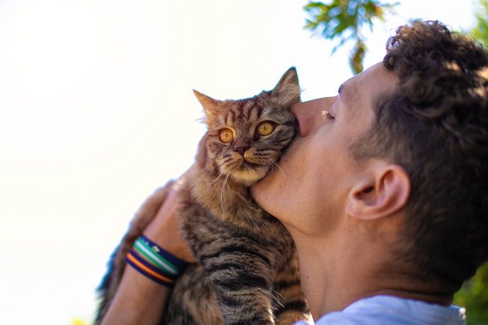 Hombre en el jardín abrazando y besando a un gato.