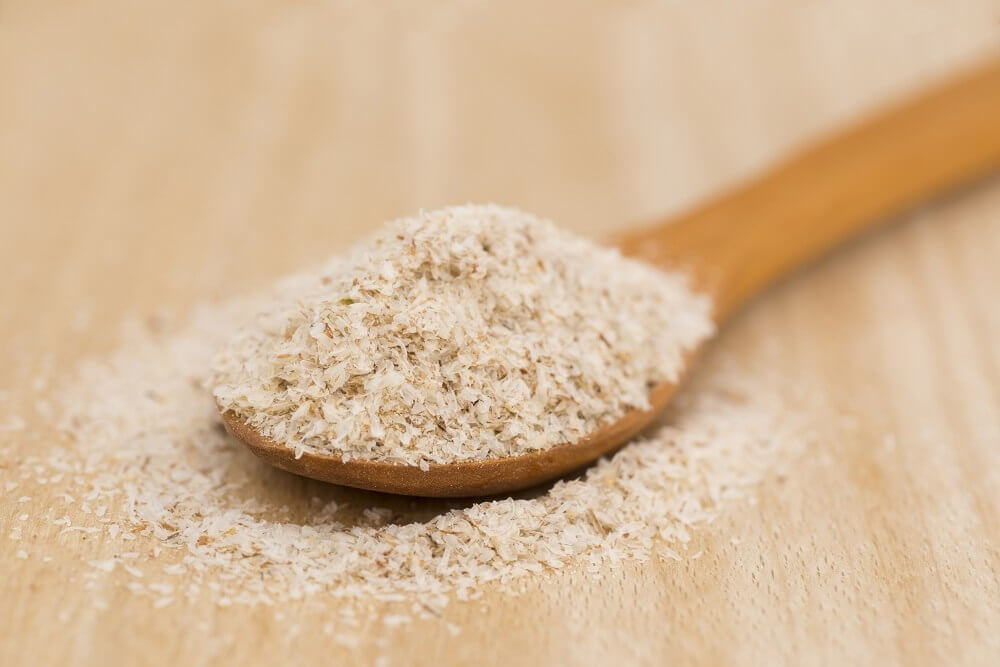 Cuchara de madera con semillas de psyllium sobre fondo de madera